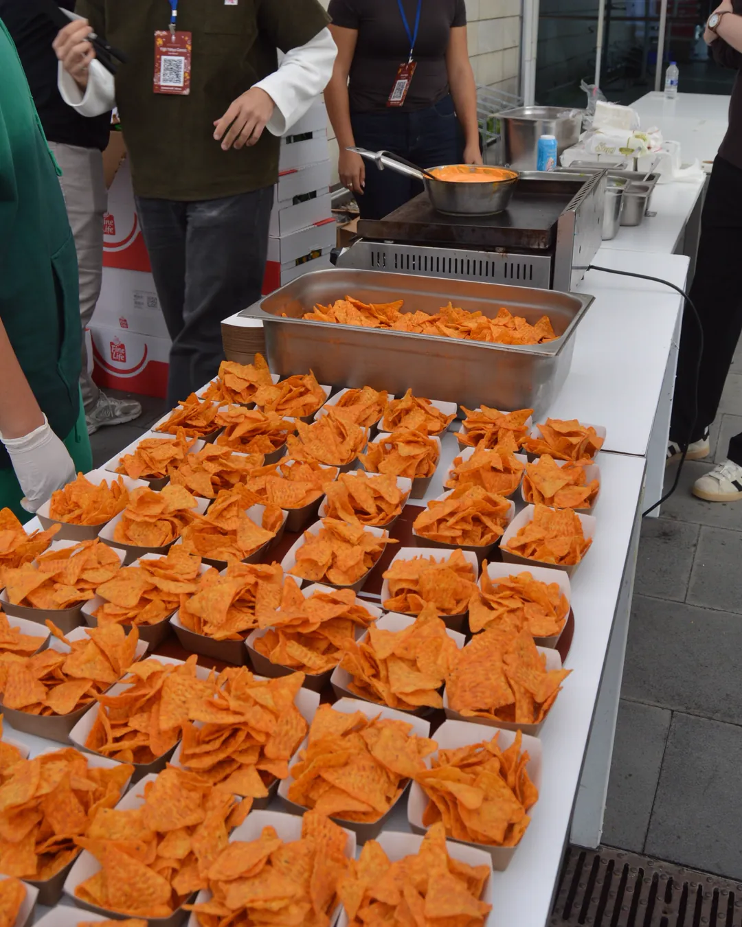 Kulübün nachos standı: kâğıt kaselere dizilmiş yüzlerce nachos, arkada ocak başında ekip